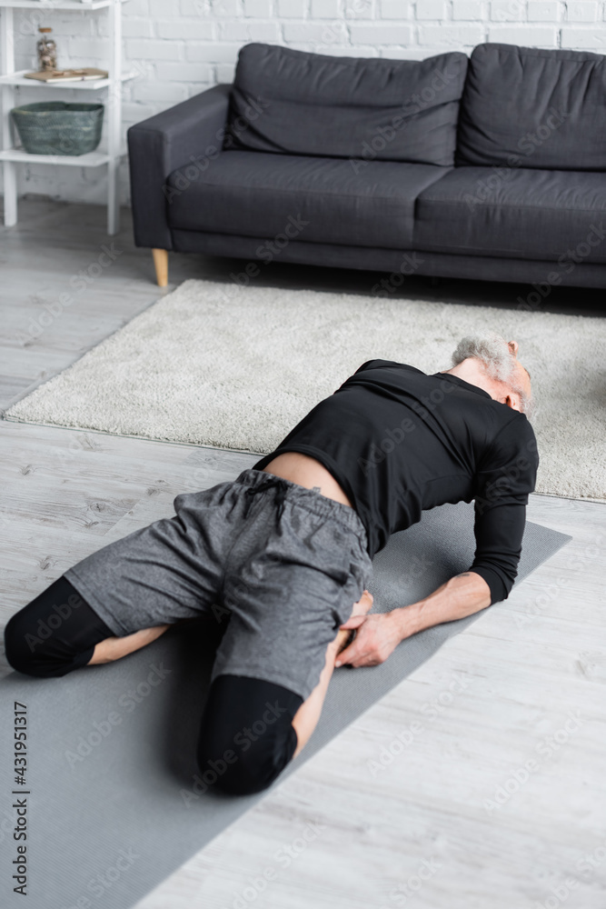bearded man in sportswear stretching on fitness mat in living room. bearded man in sportswear stretching on fitness mat in living room.
