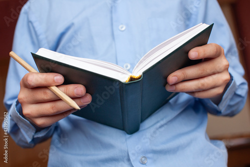 children hands holding notebook in green cover and pencil on background of blue shirt, selective focus