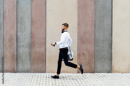 Businessman holding briefcase and jacket while running against wall