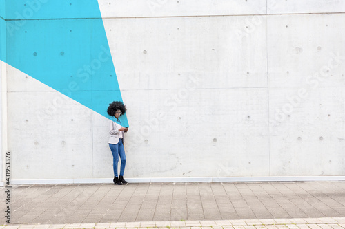 Young woman standing outdoors with smart phone in hands covered in blue facial recognition effect photo