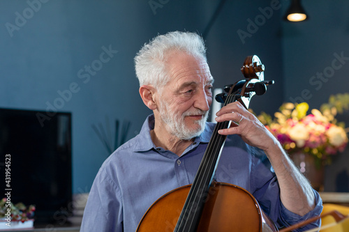 Smiling senior man playing cello at home