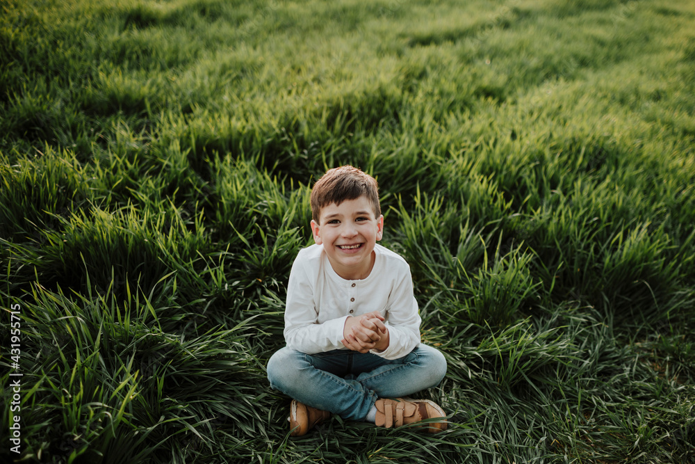 Cheerful boy with hands clasped sitting at grassy field Cheerful boy with hands clasped sitting at grassy field