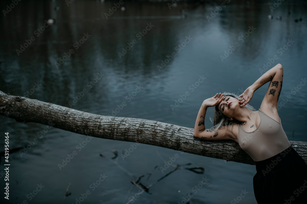 © Gala Mart√≠nez L√≥pez/Westend61 - Young woman with eyes closed leaning on fallen tree against lake