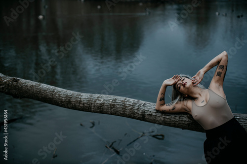 Young woman with eyes closed leaning on fallen tree against lake photo