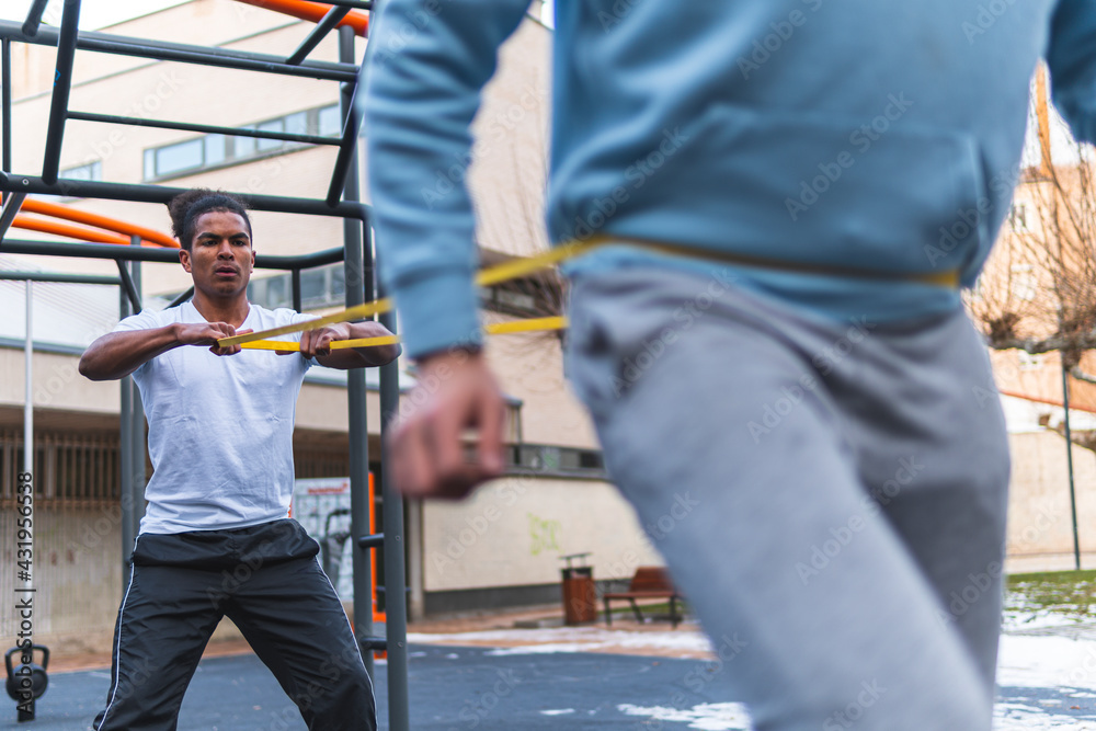 Young man holding stretching band while exercising with friend in city Young man holding stretching band while exercising with friend in city