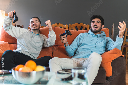 Young competitive friends playing video game sitting on sofa in living room photo