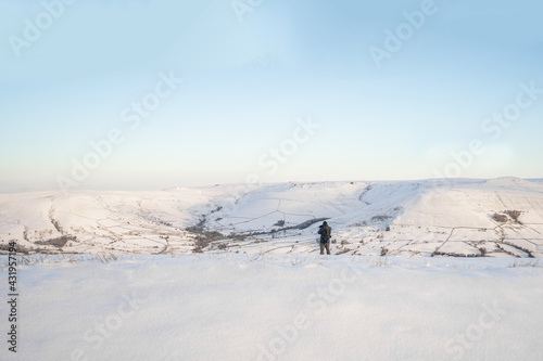 Lone mountain explorer stood out in the snow capped hills looking at view and sunrise. Wrapped up warm in Peak District Derbyshire England. 