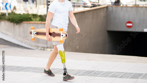 Young disabled man holding skateboard while walking on footpath