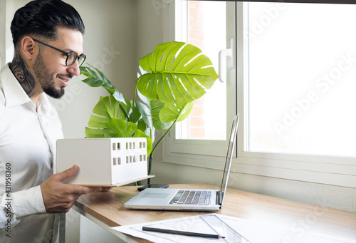 Smiling design professional showing architectural model during video call through laptop at desk photo
