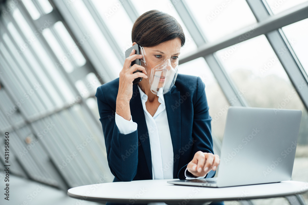 Mature businesswoman talking on smart phone while working in office during COVID-19 Mature businesswoman talking on smart phone while working in office during COVID-19