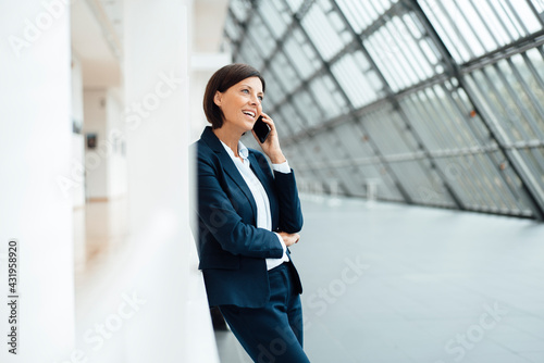 Businesswoman talking on smart phone while leaning on wall in corridor photo