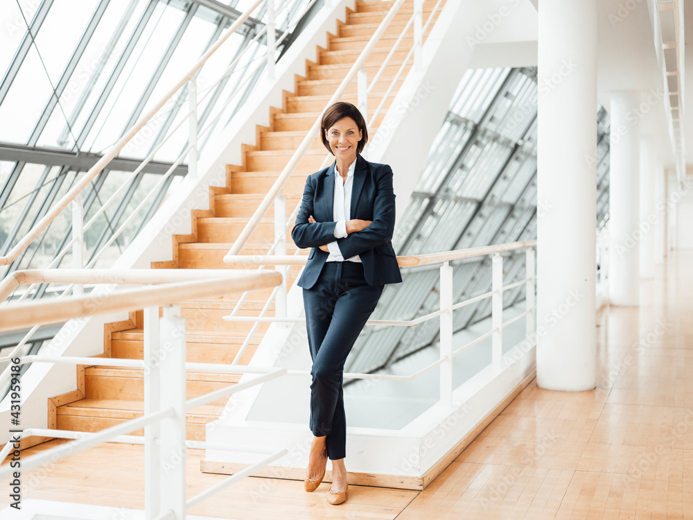 Smiling confident businesswoman with arms crossed by railing in corridor Smiling confident businesswoman with arms crossed by railing in corridor