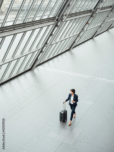 Mature businesswoman with suitcase walking at corridor