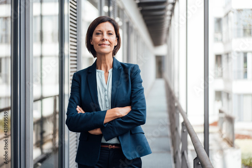 Smiling confident businesswoman with arms crossed standing on balcony