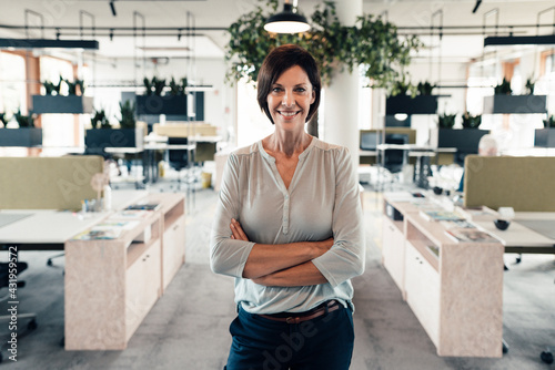 Confident businesswoman with arms crossed standing in office photo