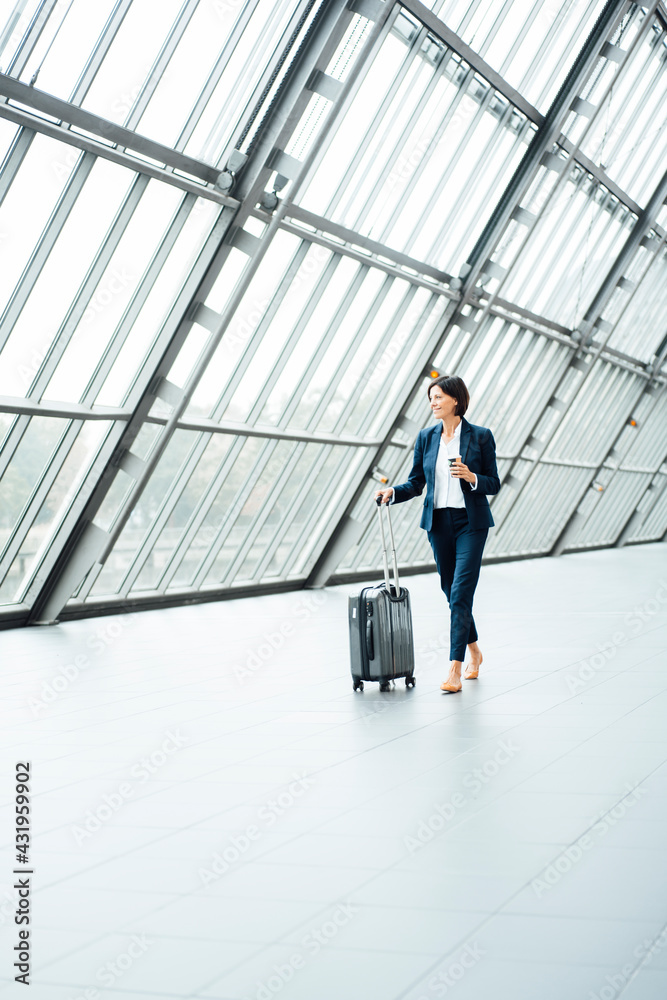 Female entrepreneur with suitcase looking away while walking in corridor Female entrepreneur with suitcase looking away while walking in corridor
