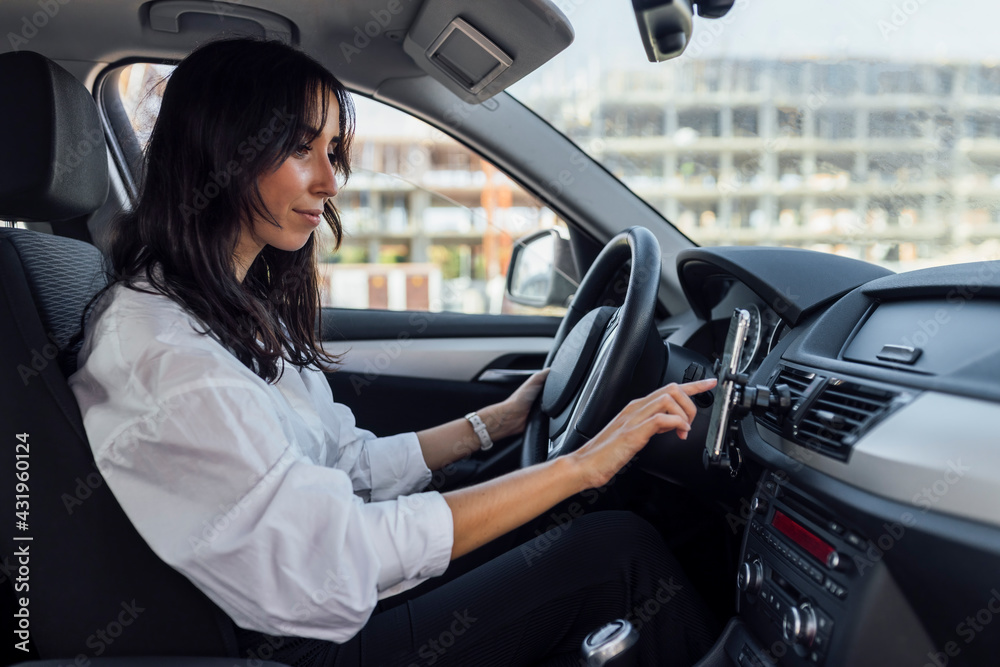 © Julio Rodriguez/Westend61 - Young woman setting up global positioning system through smart phone while sitting in car
