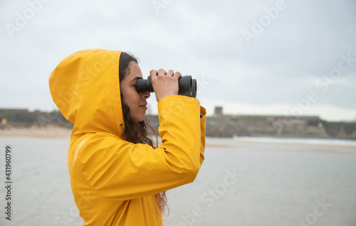 Young woman looking through binoculars while standing at beach
