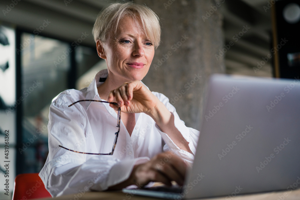 © Robijn Page/Westend61 - Smiling businesswoman holding eyeglasses while working on laptop at home office © Robijn Page/Westend61 - Smiling businesswoman holding eyeglasses while working on laptop at home office