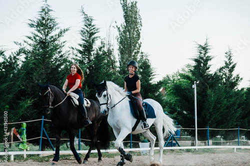 Happy female friends riding horses in farm