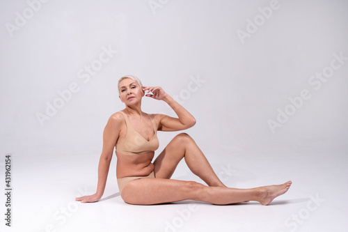 Senior woman wearing lingerie staring while sitting against gray background