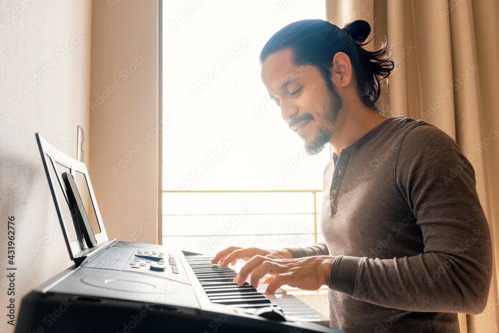 Young latin man learning to play piano at home in the living room with a  window light Stock Photo | Adobe Stock
