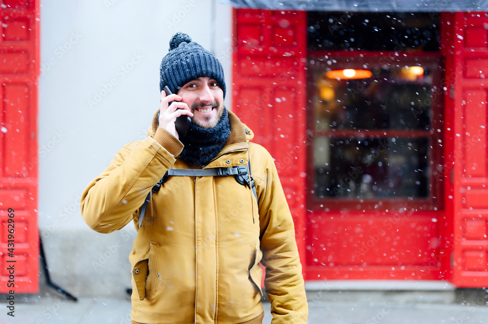 Smiling man talking on mobile phone while standing against store during winter Smiling man talking on mobile phone while standing against store during winter