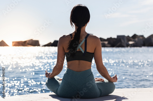 Young woman practicing lotus position on promenade during sunny day