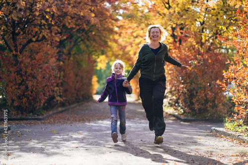 Happy mother and daughter holding hands and running in park during autumn photo