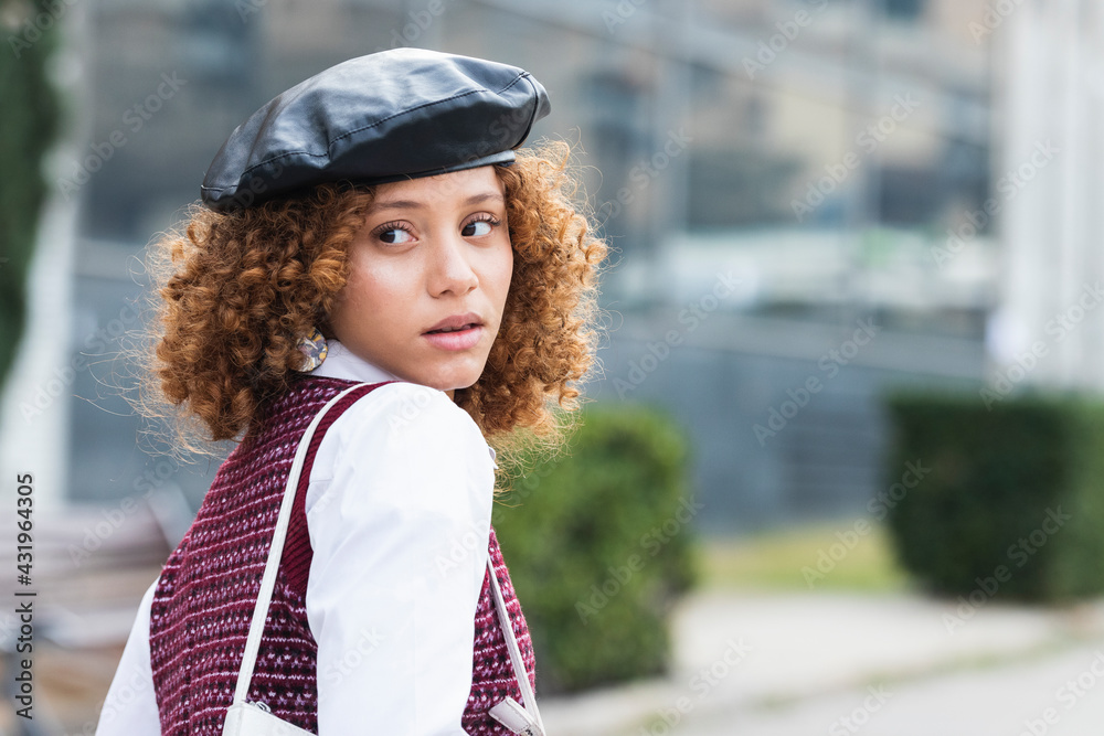Curly hair teenage girl wearing beret looking over shoulder while standing outdoors Curly hair teenage girl wearing beret looking over shoulder while standing outdoors