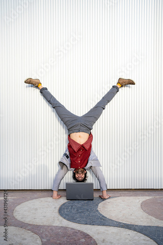 Businessman looking at laptop while doing handstand in front of wall