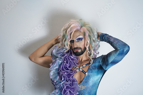 Drag queen with hand in hair standing against white wall