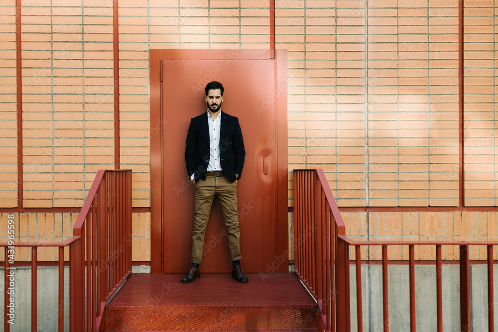 Businessman staring while standing with hands in pockets against door Businessman staring while standing with hands in pockets against door