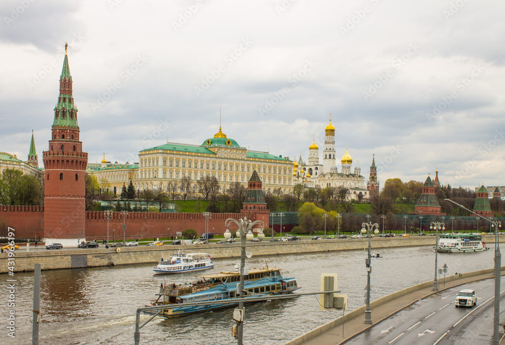 Fototapeta premium Moscow / Russia - May, 5, 2021: view of the brick wall, the yellow Grand Kremlin Palace and the Assumption Cathedral with golden domes on the banks of the Moskva River on a cloudy spring day