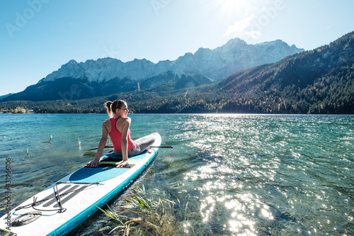 Germany, Bavaria, Garmisch Partenkirchen, Young woman sitting on stand up paddle board on Lake Eibsee and lookingat Zugspitze Mountain photo