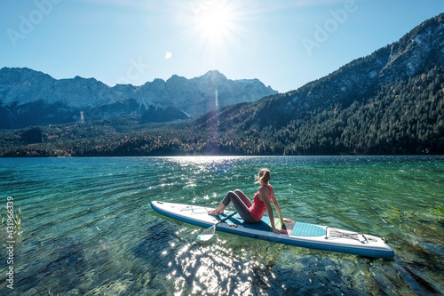 Germany, Bavaria, Garmisch Partenkirchen, Young woman sitting on stand up paddle board on Lake Eibsee and looking at Zugspitze Mountain photo