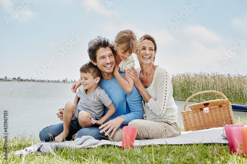 Happy family sitting in a line on blanket by lake photo