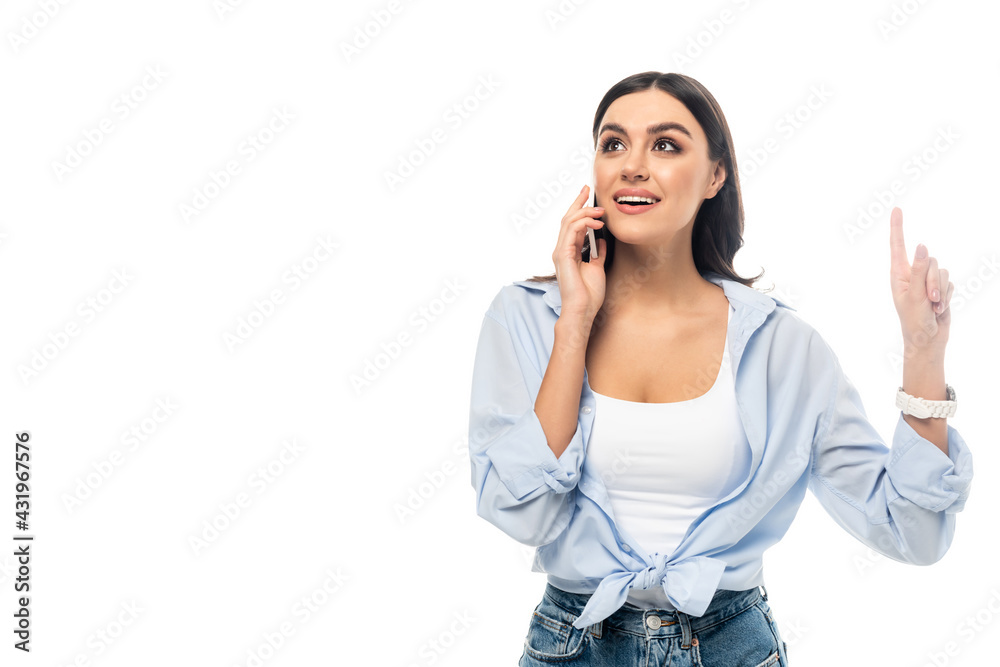 excited woman pointing up with finger while talking on cellphone isolated on white.