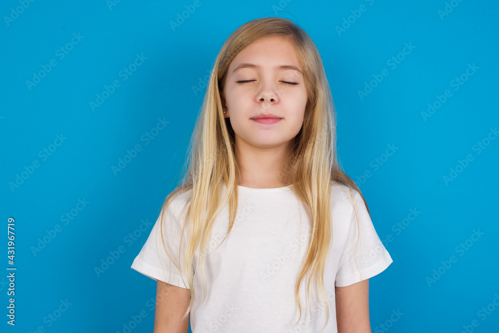 beautiful Caucasian little girl wearing white T-shirt over blue background nice-looking sweet charming cute attractive lovely winsome sweet peaceful closed eyes beautiful Caucasian little girl wearing white T-shirt over blue background nice-looking sweet charming cute attractive lovely winsome sweet peaceful closed eyes