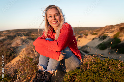 Young woman hugging knees while sitting on sand dune photo