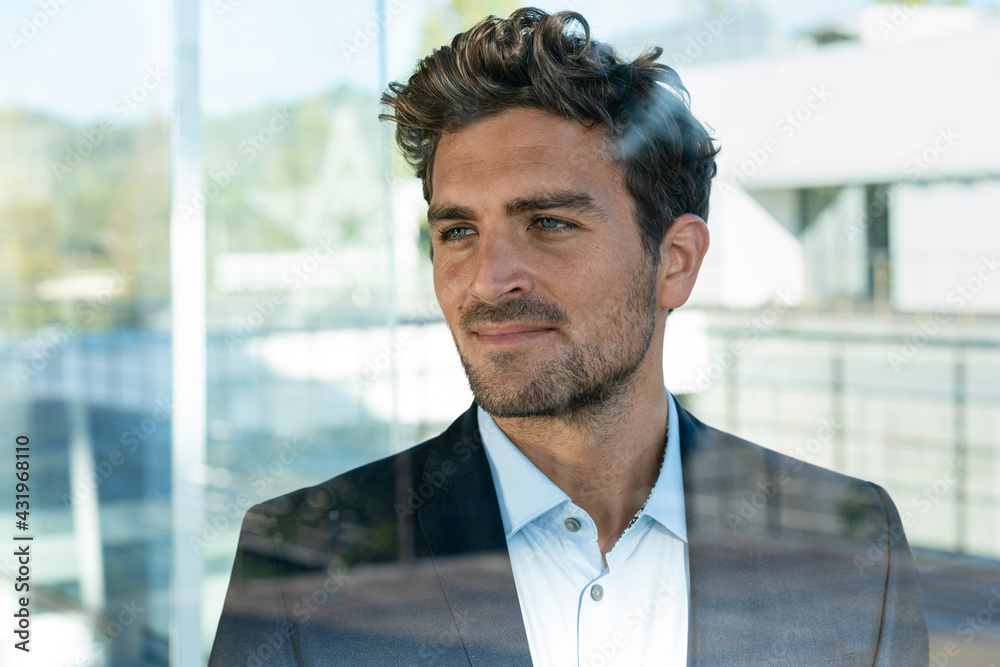 Businessman looking away while standing by window at office Businessman looking away while standing by window at office