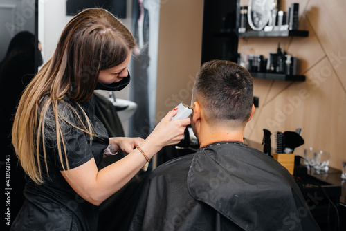 A professional stylist in a modern stylish barbershop shaves and cuts a young man's hair. Beauty salon, hair salon