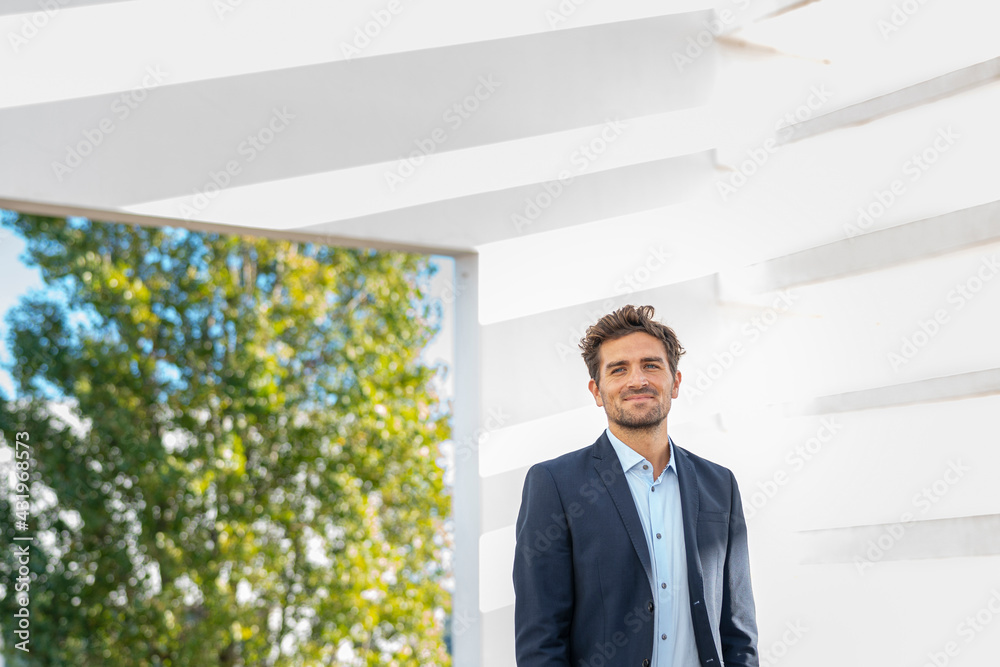 Smiling businessman looking away while standing against wall