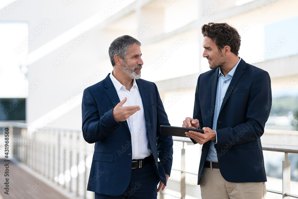 Business people discussing over digital tablet while standing at office building terrace Business people discussing over digital tablet while standing at office building terrace