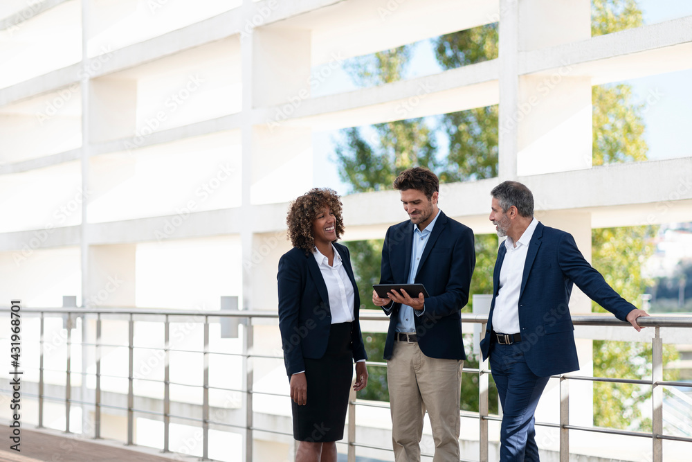 Professional team having discussion over digital tablet while standing by railing