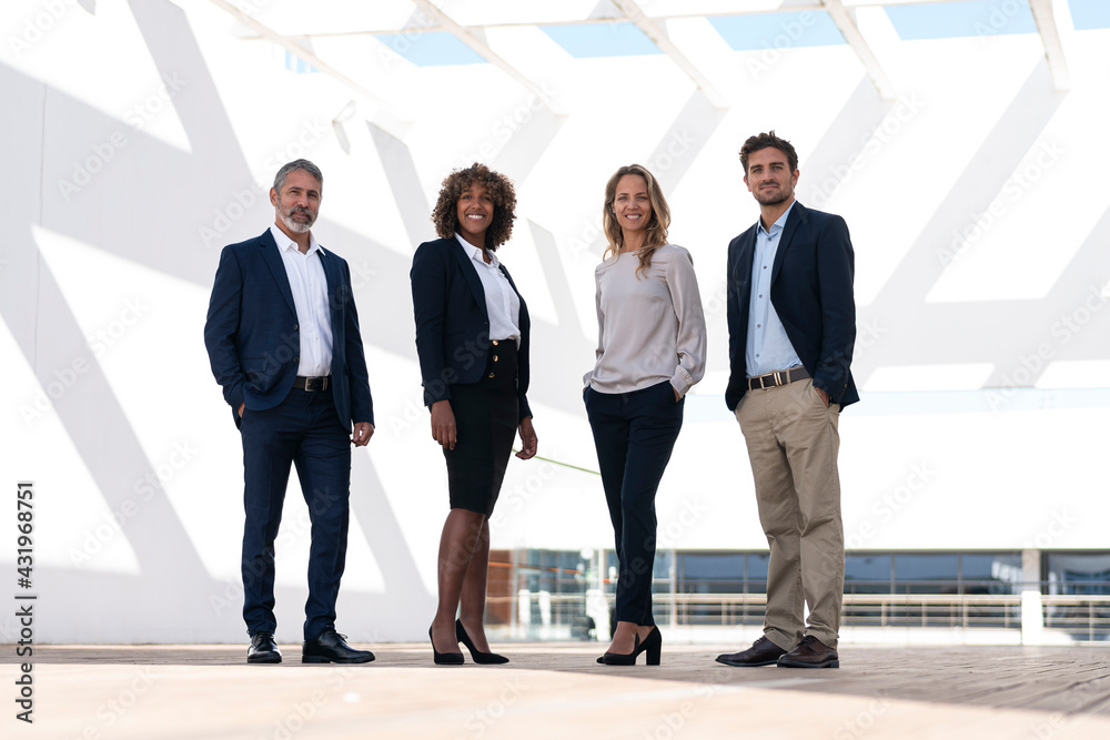 Confident business people standing with hands in pockets at office building terrace Confident business people standing with hands in pockets at office building terrace