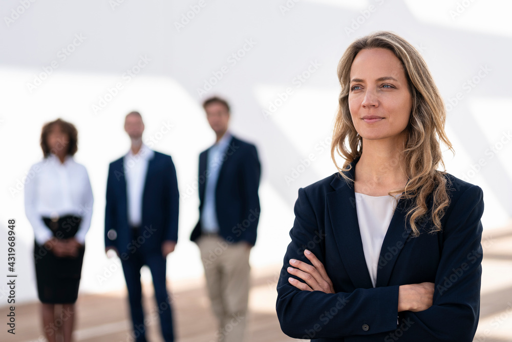 Female entrepreneur looking away while standing with colleagues in background at office terrace Female entrepreneur looking away while standing with colleagues in background at office terrace