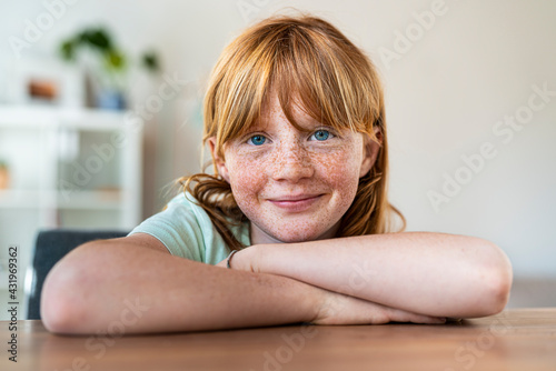 Smiling girl with arms crossed sitting at table in living room