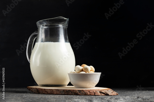 Central asian traditional kurut cheese in a white plate with a jug of fresh milk on a wooden board in low key