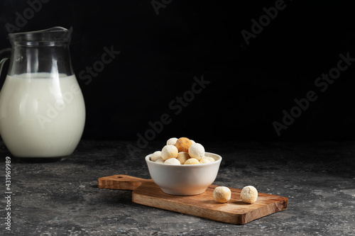 Central asian traditional cheese kurut in a white plate with a jug of fresh milk on a wooden board on a dark background photo